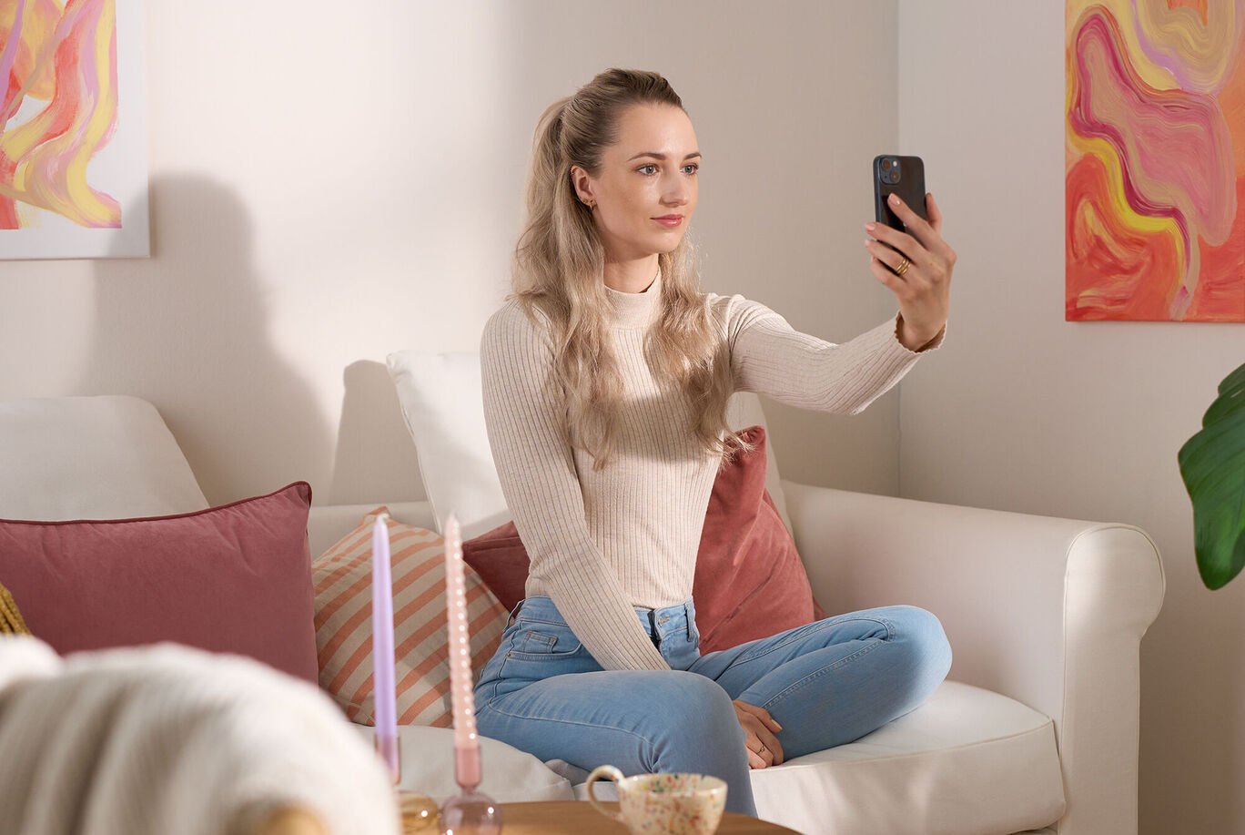 Une femme est assise confortablement sur un canapé en prenant un selfie avec son smartphone.