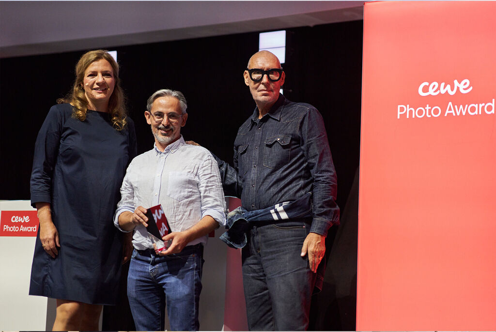 Trois personnes sont sur une scène, une personne tient un prix, la bannière CEWE Photo Award est visible en arrière-plan.
