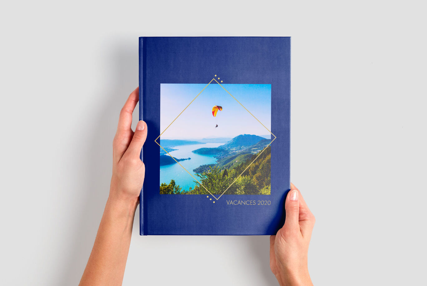 Une personne tient un livre photo CEWE avec une belle image de paysage dans les mains.