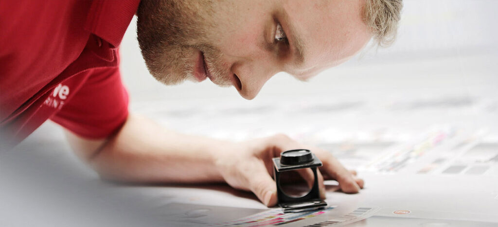 Une personne examine attentivement des matériaux d'impression à l'aide d'une loupe sur une table