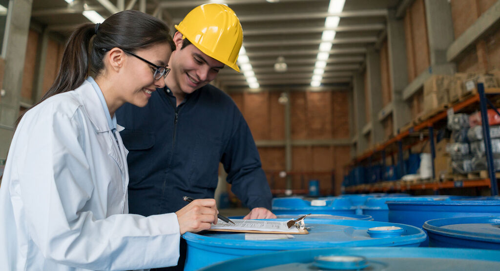 Deux travailleurs discutent d'informations importantes sur des contenants bleus dans un entrepôt.