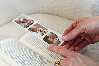 Une personne tient un collage photo avec des images d'un bébé et d'une personne âgée au-dessus d'un livre ouvert.