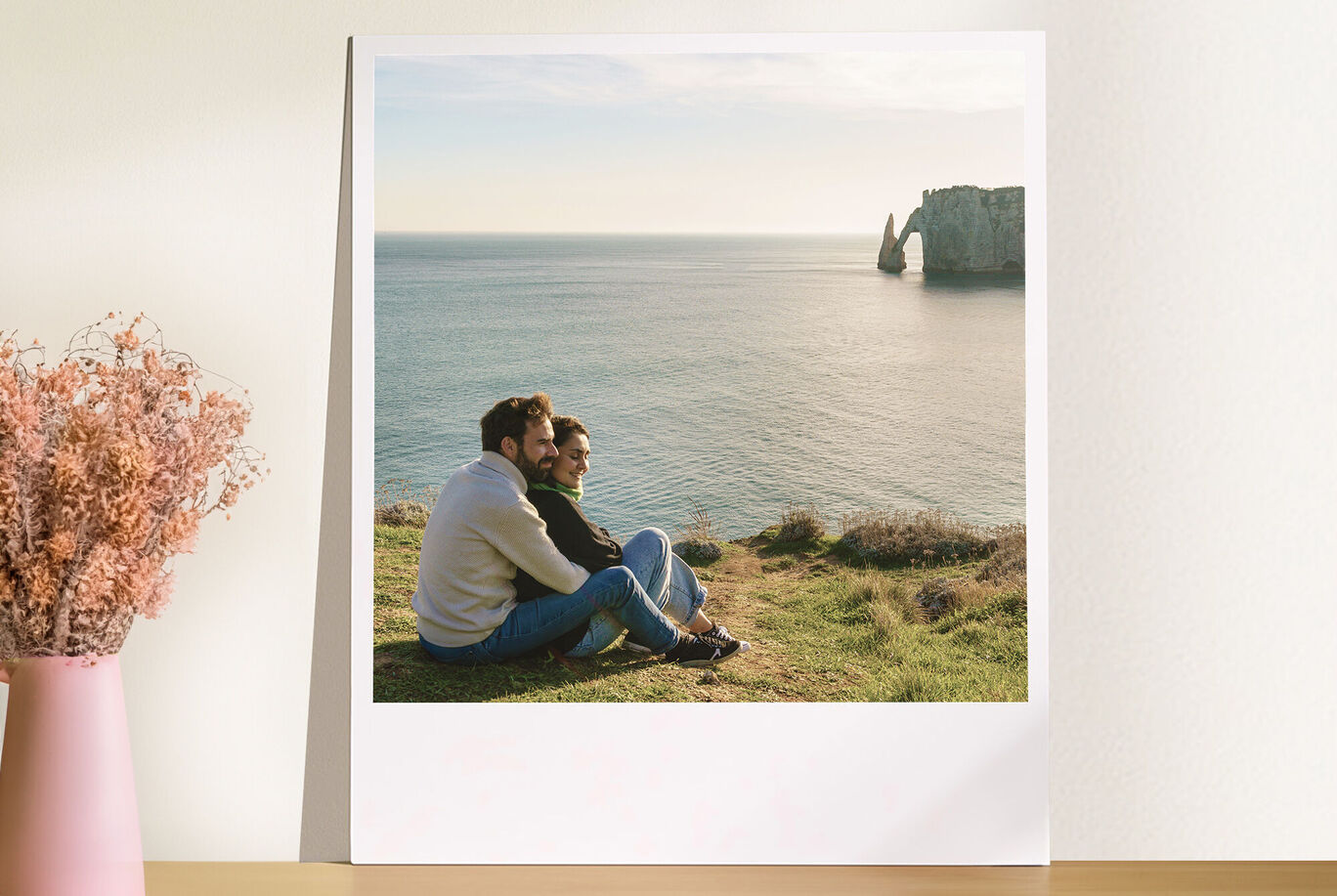 Un couple est heureux au bord de la mer sur une pelouse, entouré par la nature. On voit une falaise en arrière-plan.