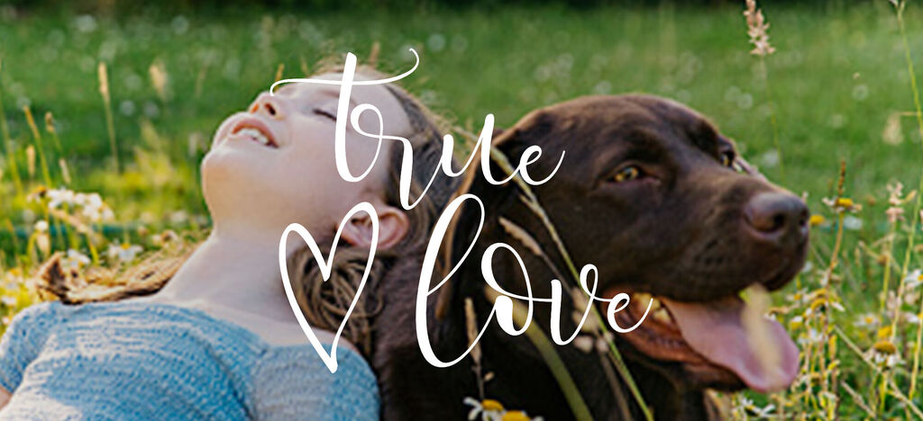 Une fille est allongée dans l'herbe, riant à côté d'un chien brun. Texte "true love" sur l'image.