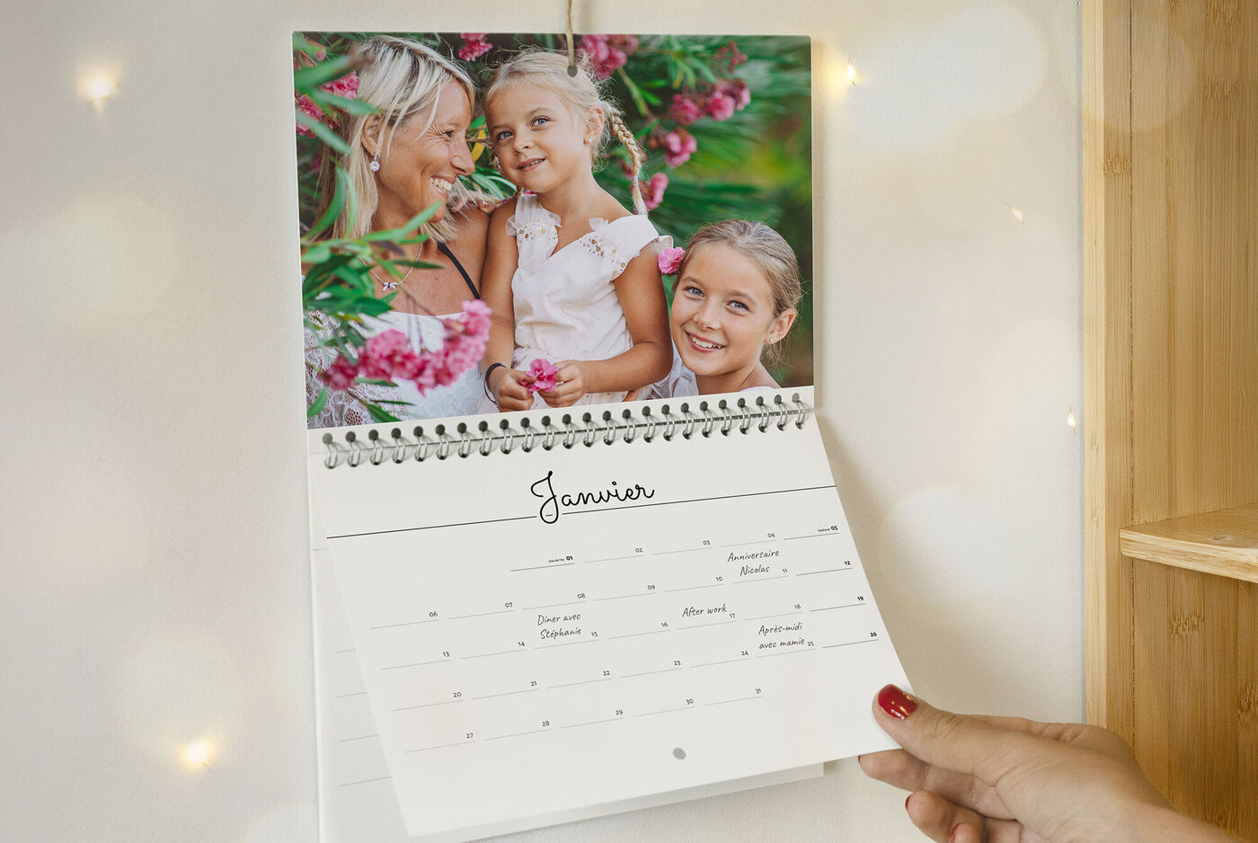 Une main tient un calendrier montrant janvier. En arrière-plan, des enfants joyeux parmi des fleurs