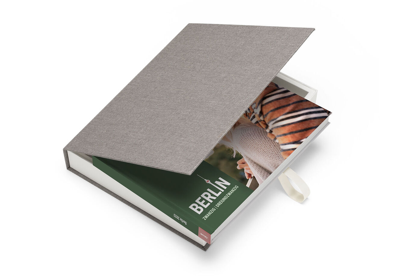 Un CEWE FOTOBUCH ouvert avec une photo de Berlin à l'intérieur et une couverture en tissu grise.