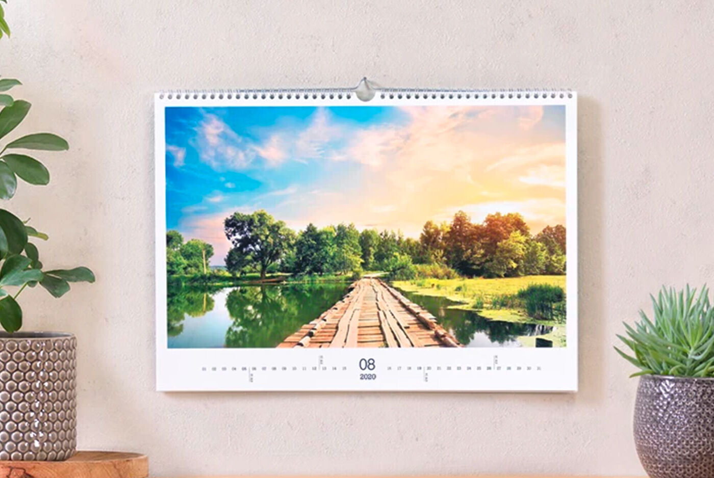 Un beau calendrier photo accroché au mur. Août montre un pont en bois pittoresque au-dessus d'un étang paisible.