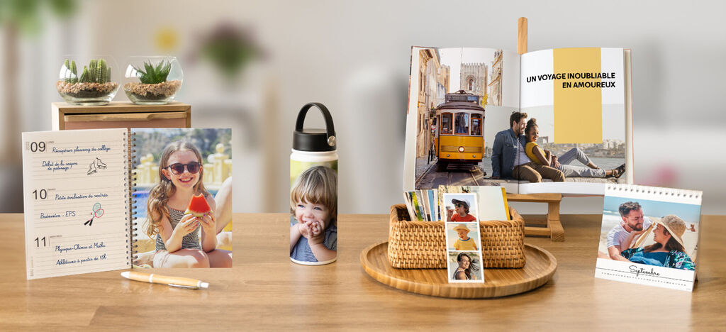 Une disposition élégante de produits CEWE personnalisés sur une table: calendrier photo, album photo, bouteille avec photo, souvenirs.