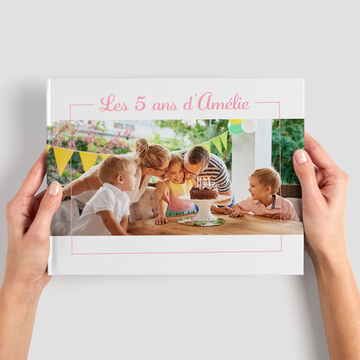 Une personne montre un album photo CEWE avec une couverture colorée pour un anniversaire d'enfants.