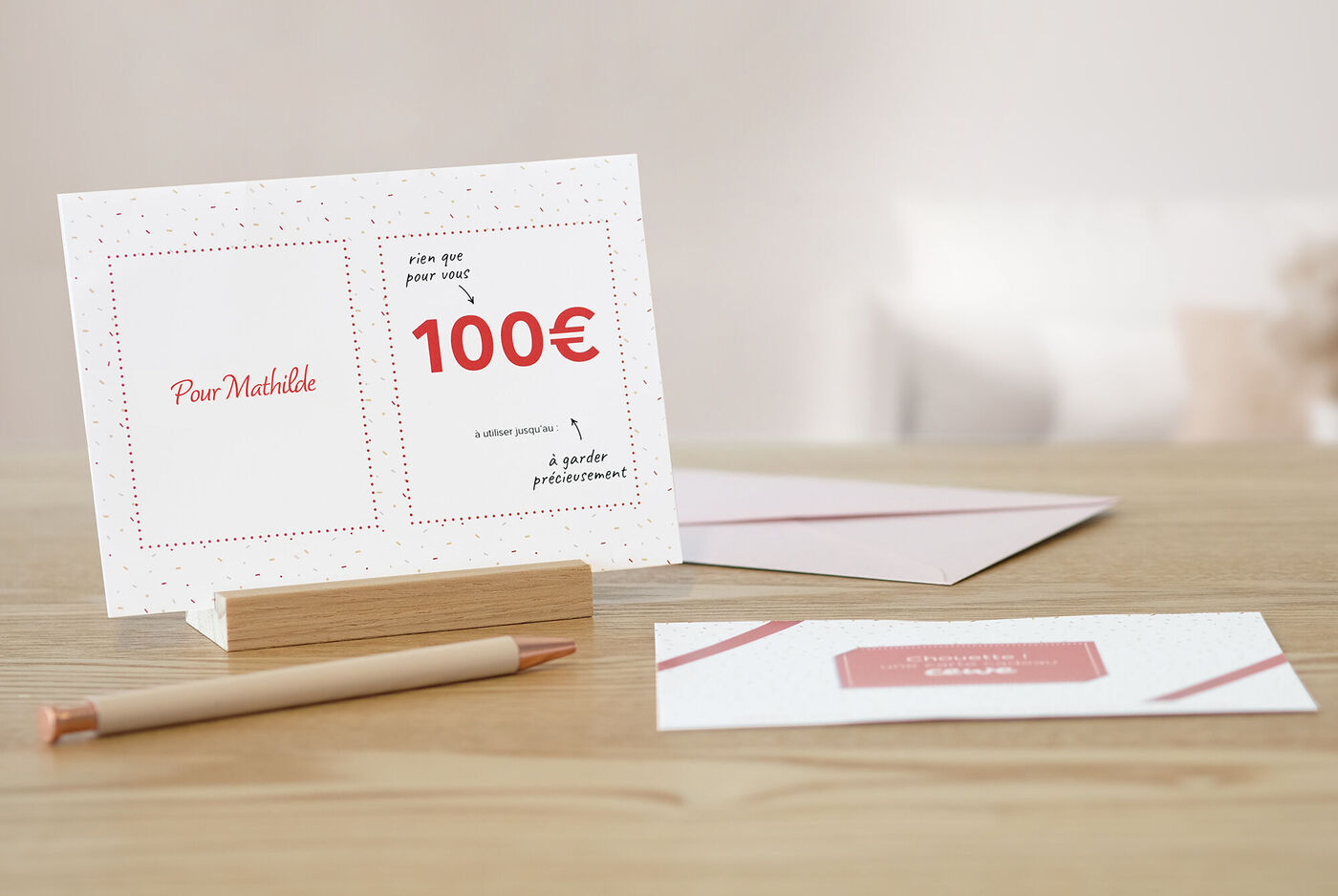 Cartes de vœux CEWE avec un bon de 100 euros au design élégant, entourées d'une enveloppe et d'un crayon sur un fond en bois.