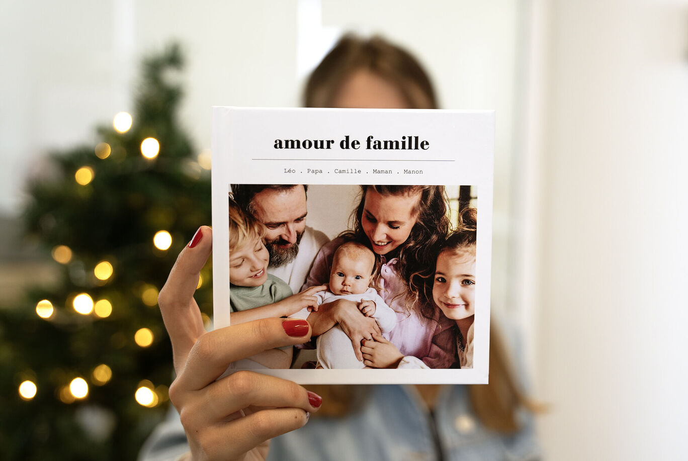 Une personne tient un album photo avec une photo de famille. L'album montre des moments joyeux et des souvenirs affectueux. Arrière-plan avec un beau sapin de Noël décoré.