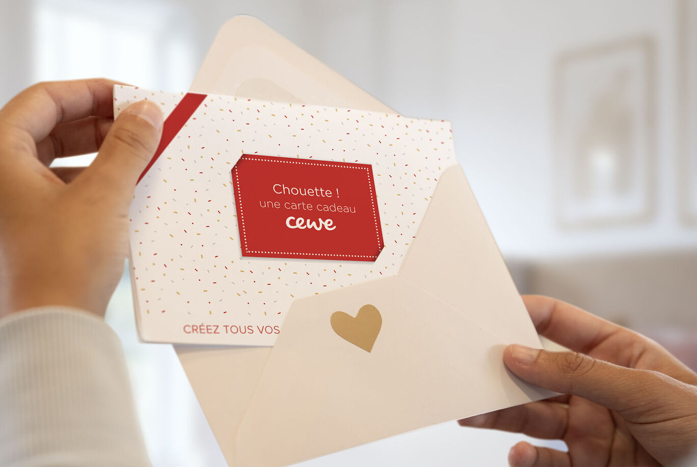 Une personne tient une carte CEWE dans une enveloppe avec motif cœur.