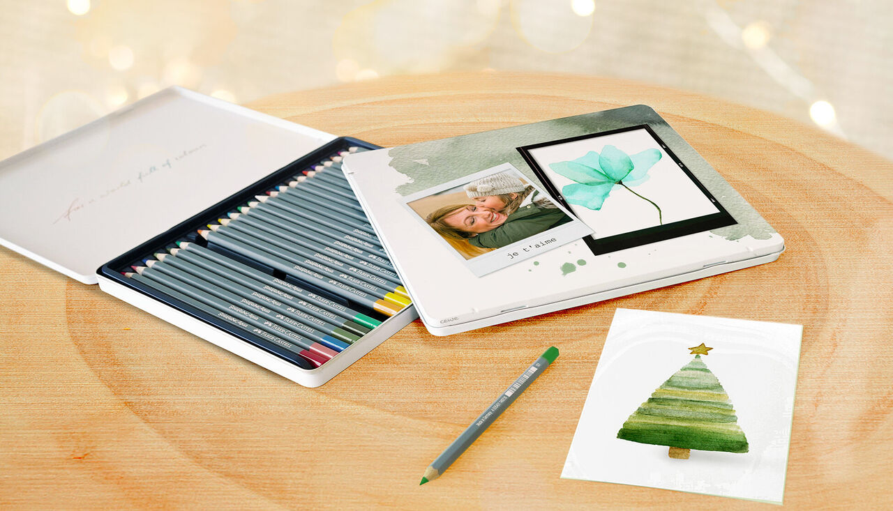 Une boîte de cadeau créative avec des crayons de couleur et une photo personnelle. Carte de Noël peinte à l'aquarelle à côté.