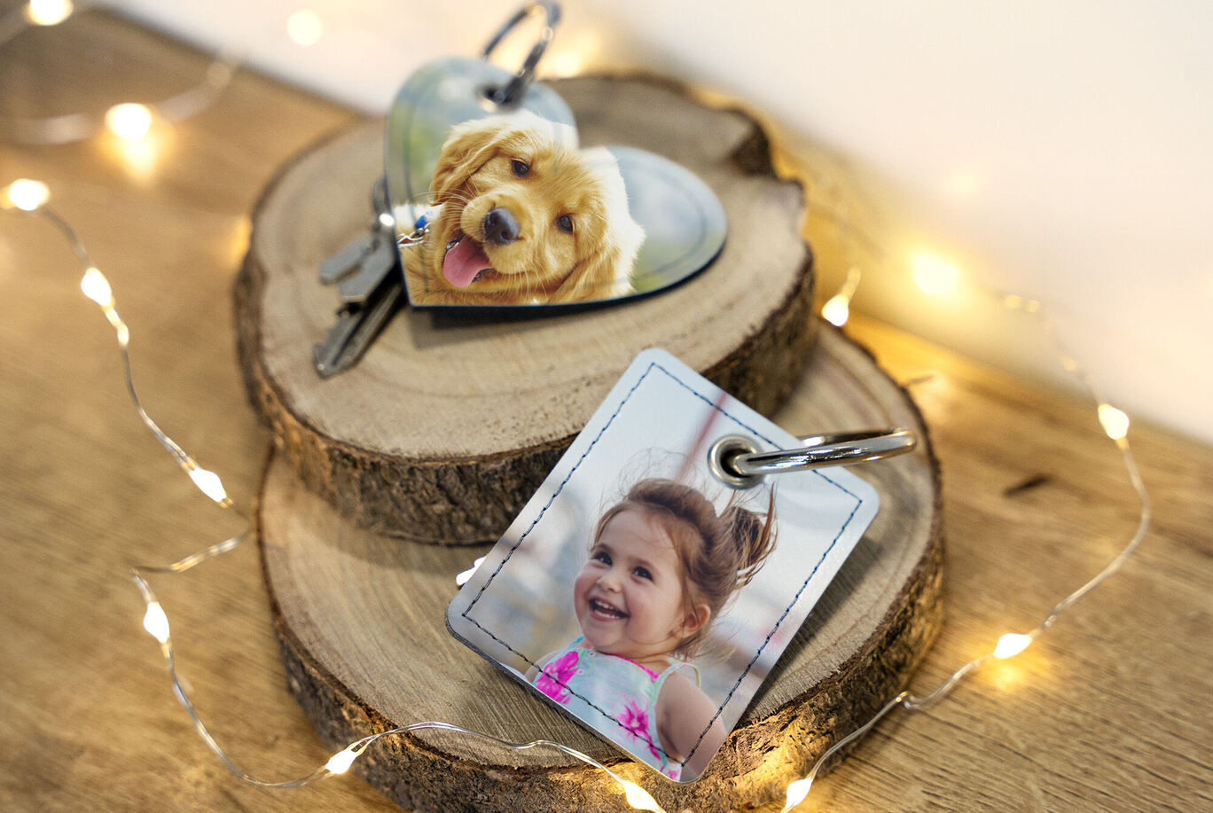 Deux porte-clés personnalisés sur un support en bois, l'un en forme de cœur avec une photo de chien et l'autre carré avec une photo de personne, entourés de lumières.