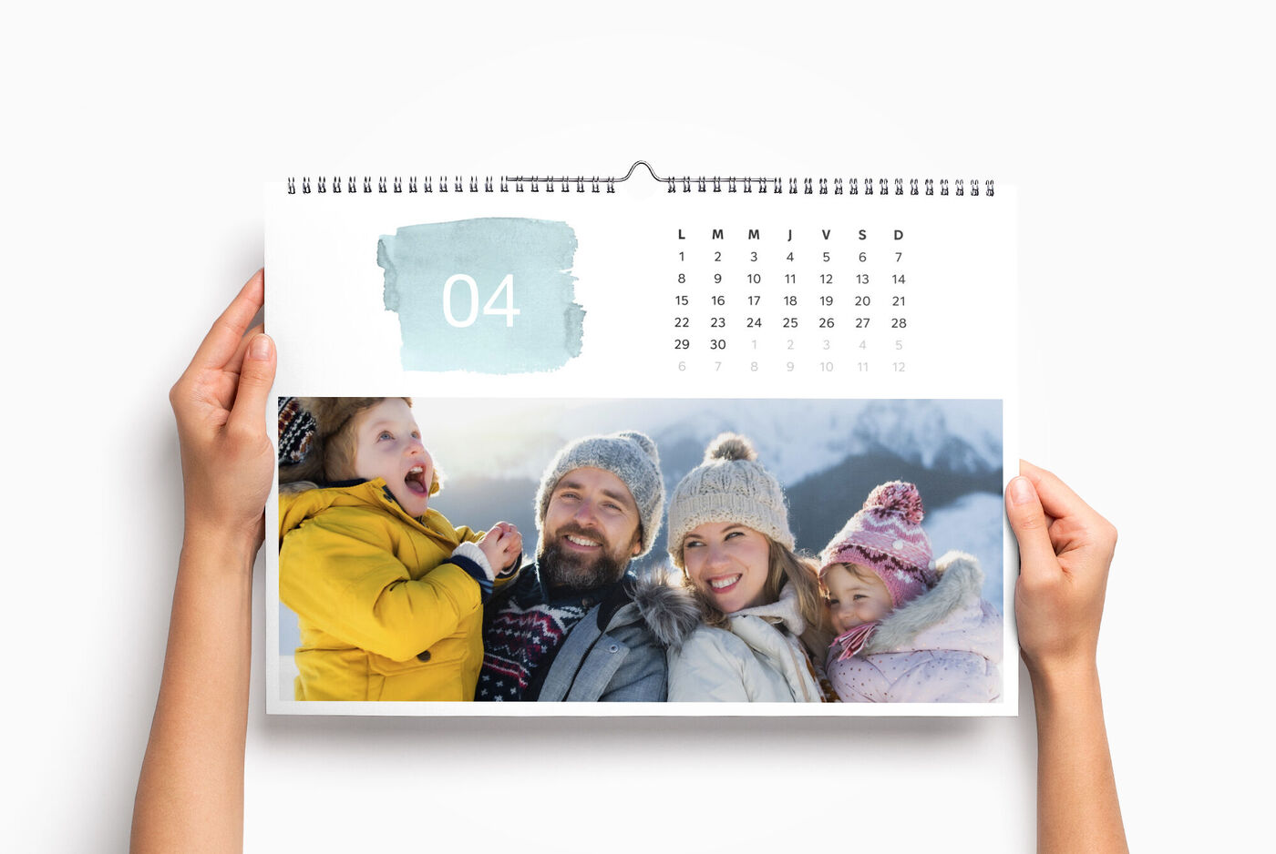 Un grand calendrier personnalisé paysage entre les mains d'une personne, avec la photo d'une famille l'hiver