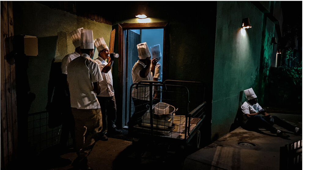 Des chefs cuisinent dans une cuisine sombre, tandis qu'un est assis par terre.