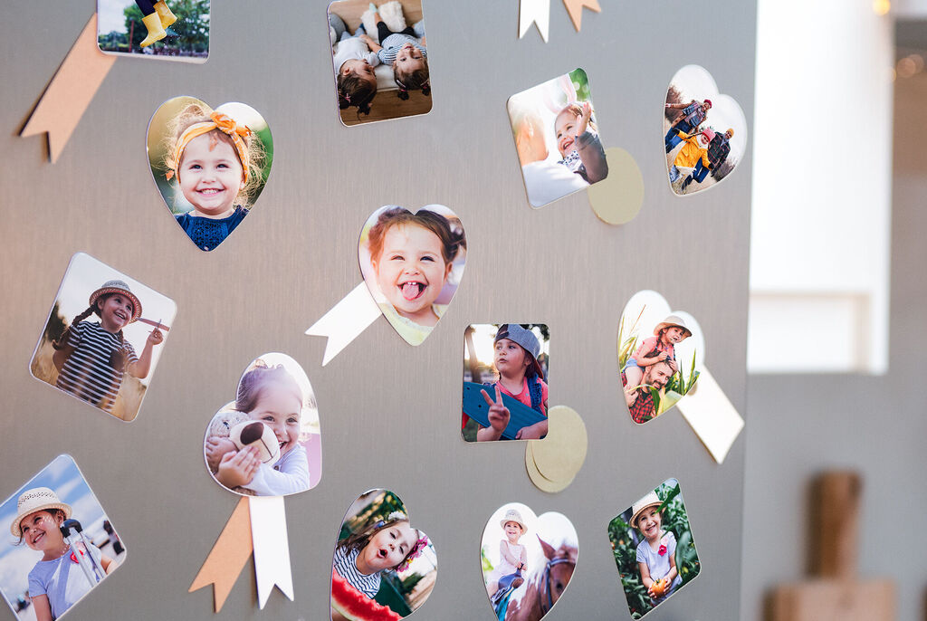 Des photos colorées en forme de cœur suspendues à un mur avec des rubans.