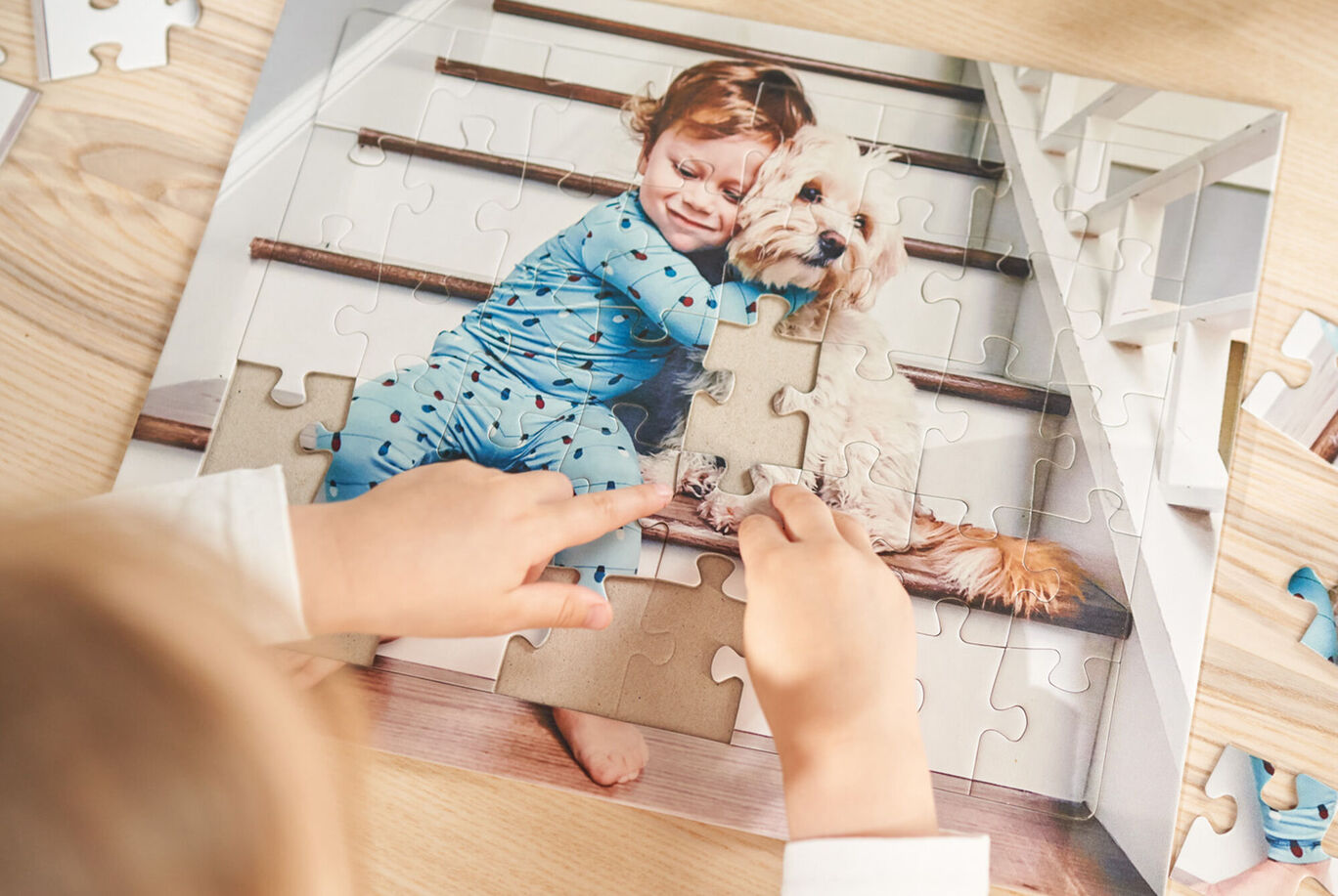 Un enfant en pyjama bleu assemble un puzzle avec un chien sur des escaliers.