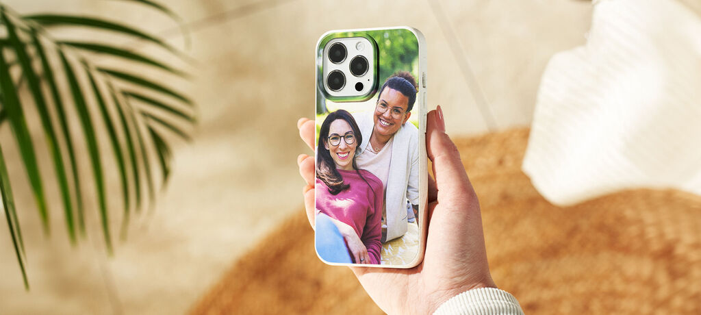 Main tenant un smartphone avec une coque personnalisée montrant une belle photo d'une famille heureuse.