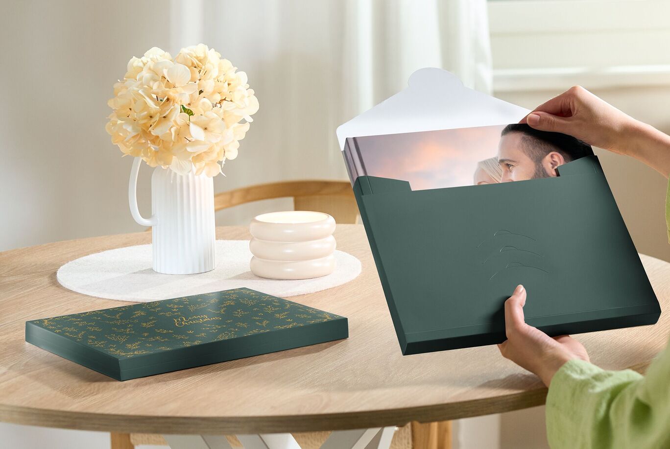 Une personne tient un album photo sombre avec une belle couverture sur une table avec des fleurs et des barres.