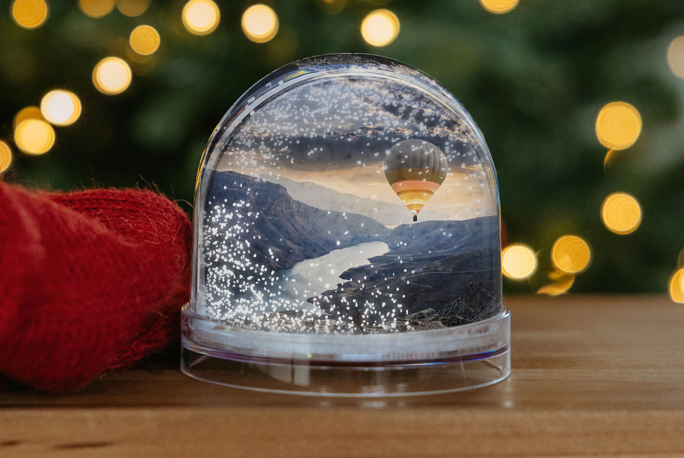 Boule à neige avec paysage de montagne et montgolfière devant des arrière-plans lumineux.