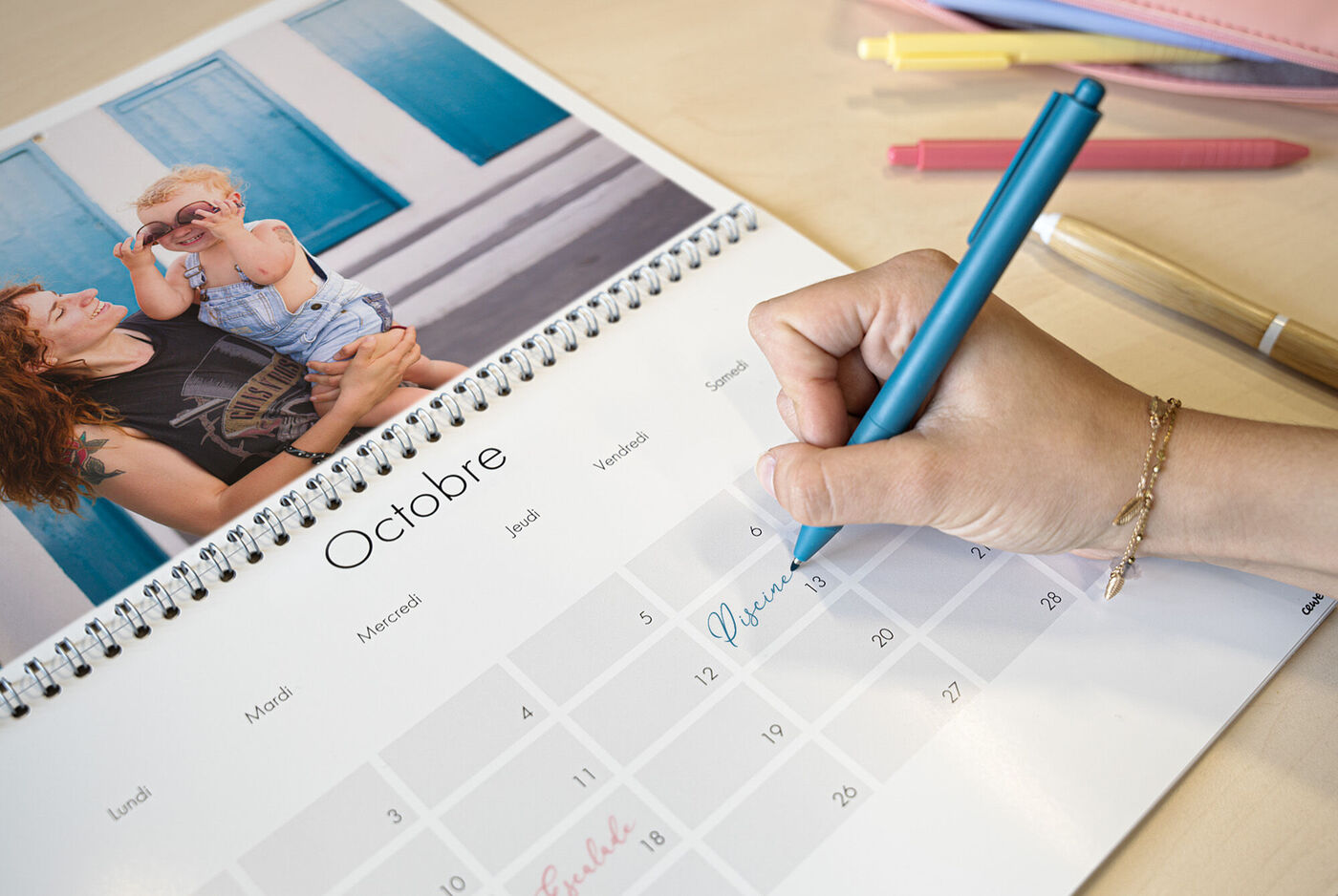 Une personne écrit dans un calendrier photo CEWE avec une photo de famille.