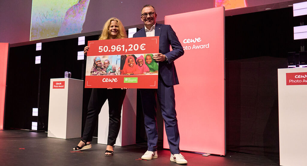Deux personnes tiennent un grand panneau de prix de 50.961,20 euros au CEWE Photo Award.