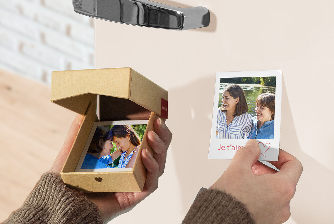 Une personne tient une petite boîte-cadeau avec une photo et montre une autre photo avec un message affectueux. La scène dégage joie et souvenirs.