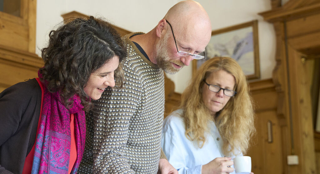 Trois personnes dans une pièce confortable regardent quelque chose ensemble avec intérêt. Ambiance positive.