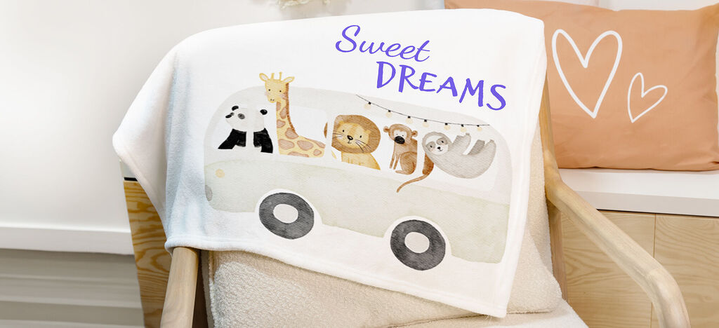 Une douce couverture pour enfant blanche avec un motif animal coloré montre une voiture avec des animaux et écrit "Sweet Dreams".