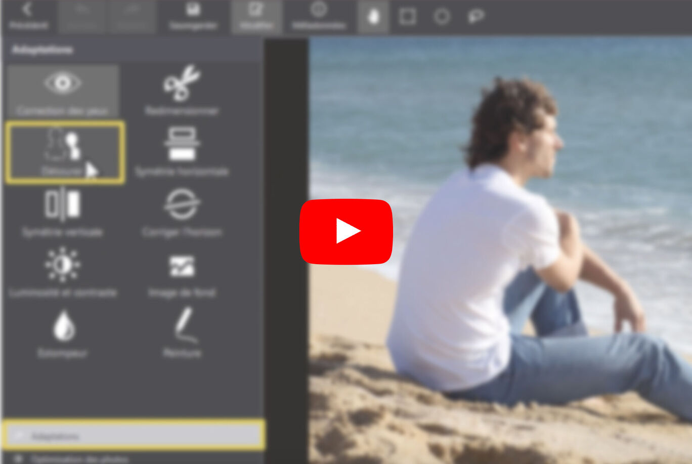 Un garçon assis sur la plage regarde l'eau. En arrière-plan, on voit la mer et le ciel.