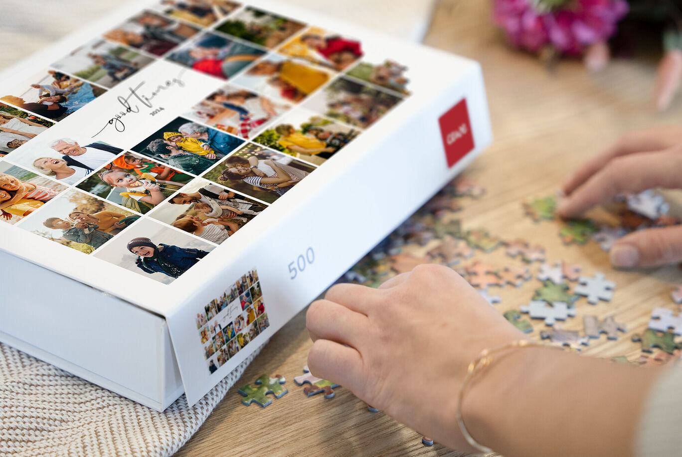 Une main place des pièces de puzzle sur une table à côté d'une boîte de 500 pièces décorée de photos.
