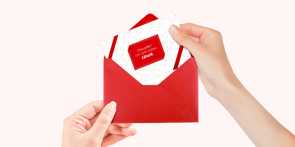 Une personne tient une enveloppe rouge avec une carte blanche à pois et une petite étiquette rouge 'CEWE'