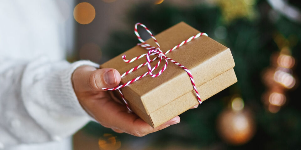 Une personne tient un cadeau soigneusement emballé avec un ruban rouge et blanc.