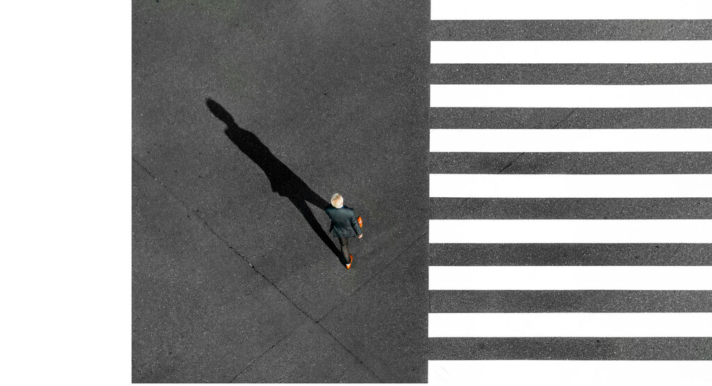 Un homme traverse un passage piéton sur un chemin en asphalte.