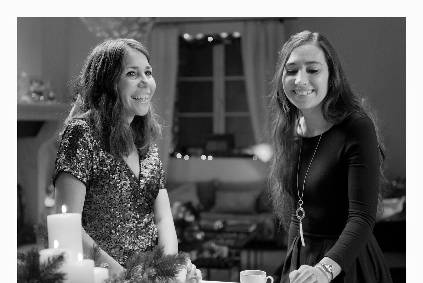 Deux femmes en vêtements de fête se tiennent ensemble, devant des bougies et une tasse, ambiance festive, convivialité.