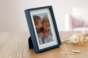 Une belle image de deux enfants s'enlaçant et s'embrassant. L'image est dans un cadre moderne bleu sur une table en bois.