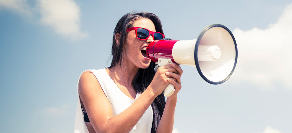 Une personne avec un mégaphone parle passionnément sous un ciel bleu.