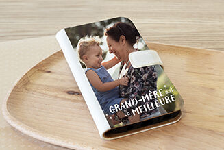 Une personne tient un album photo sur un plateau en bois, le titre indique "GRAND-MÈRE EST LA MEILLEURE".