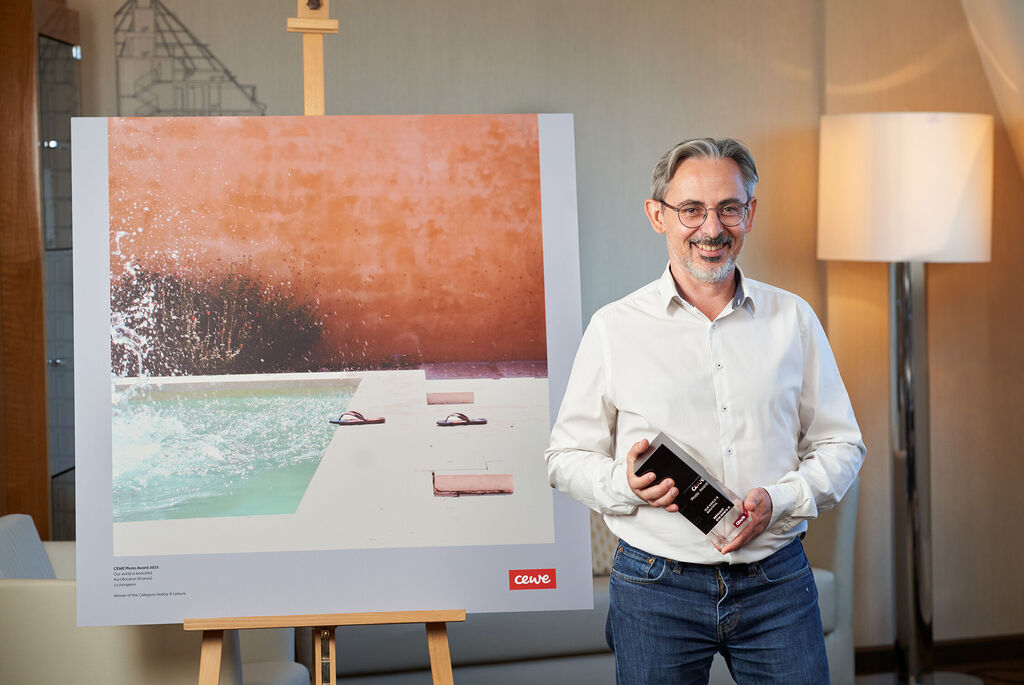 Une personne présente un appareil photo de qualité devant une grande œuvre d'art représentant une piscine. L'atmosphère est créative et inspirante.