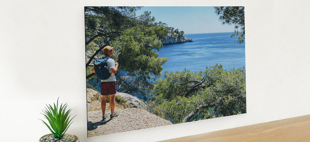 Une personne avec un sac à dos se tient sur un chemin rocheux en regardant l'eau bleue et les arbres.