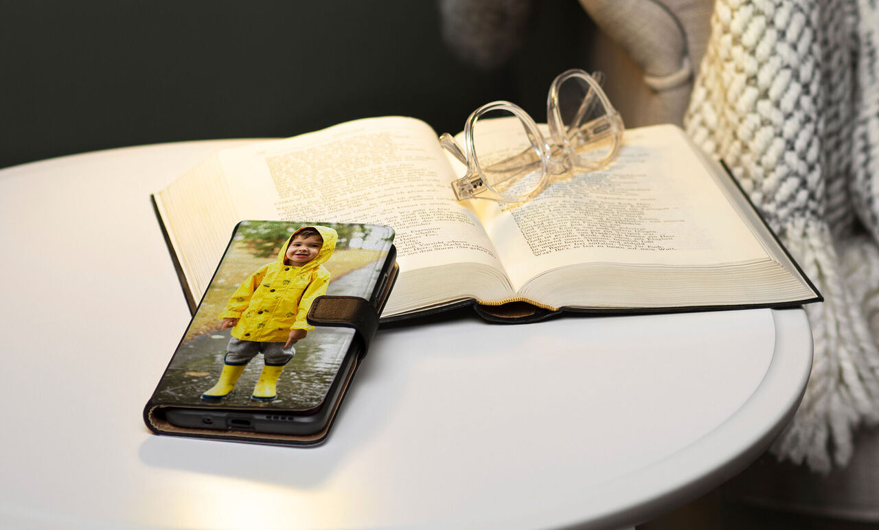 Une table élégante avec un livre ouvert et des lunettes. Un smartphone montre un enfant joyeux en imperméable jaune.