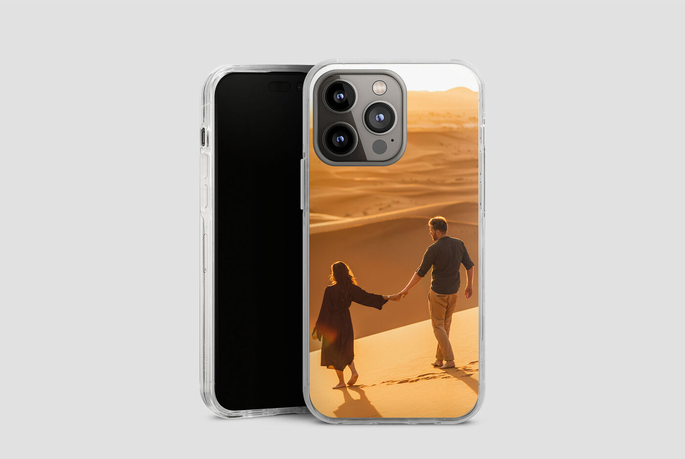 Un couple se tient par la main et marche à travers un paysage de sable au coucher du soleil, leurs silhouettes sont visibles.