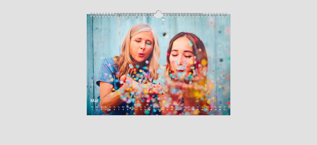Deux femmes lancent des confettis colorés dans les airs, ambiance joyeuse, calendrier CEWE.