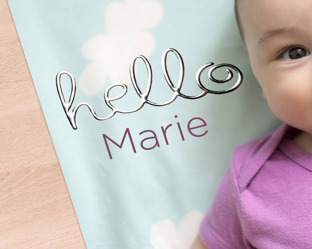 Un bébé souriant avec un t-shirt violet sur un fond bleu clair avec des nuages blancs et 'hello Marie'.