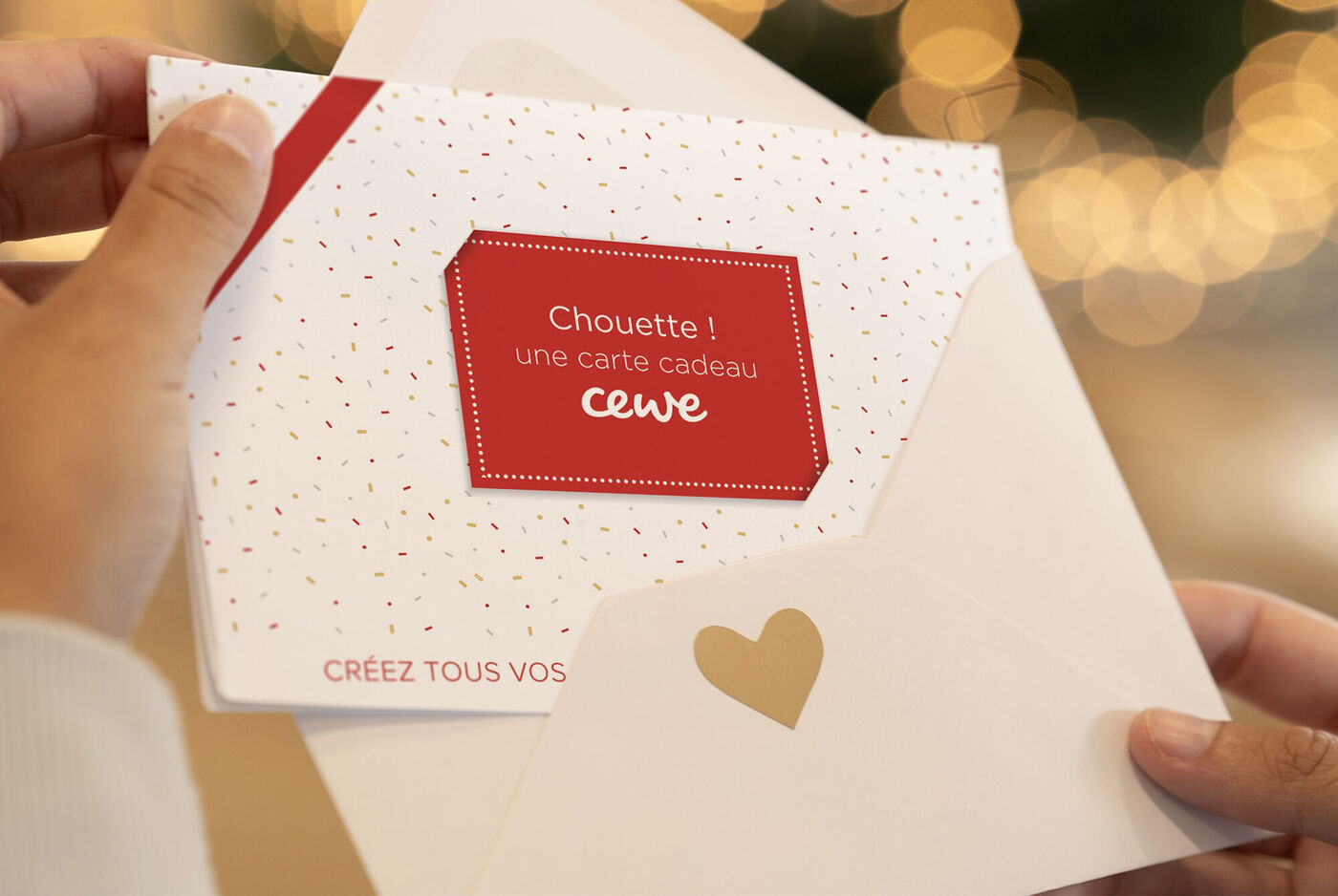 2 mains ouvrant une enveloppe contenant une carte cadeau CEWE