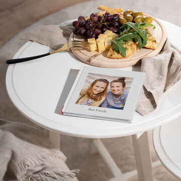 Un mini album photo carré posé sur la table avec une couverture affichant des amies