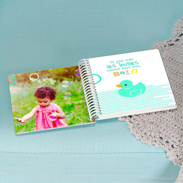 Un livre photo 14x14 cartonné pour bébé ouvert et montrant une photo d'un bébé qui fait ses premiers pages