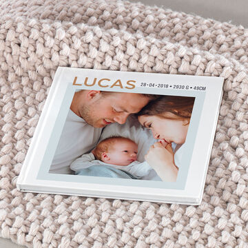 Un album photo carré avec en couverture une photo de parents avec un bébé et le prénom Lucas écrit dessus