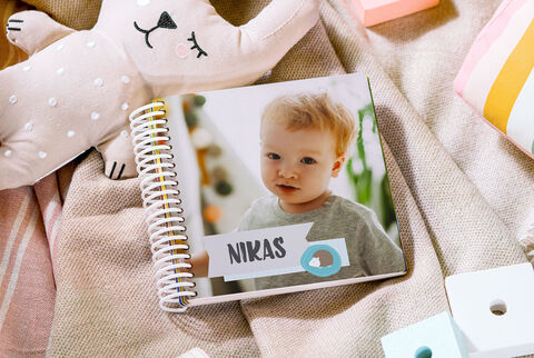 Un livre photo cartonné pour bébé fermé dont la couverture montre une image d'un enfant et écrit dessus "Nikas"